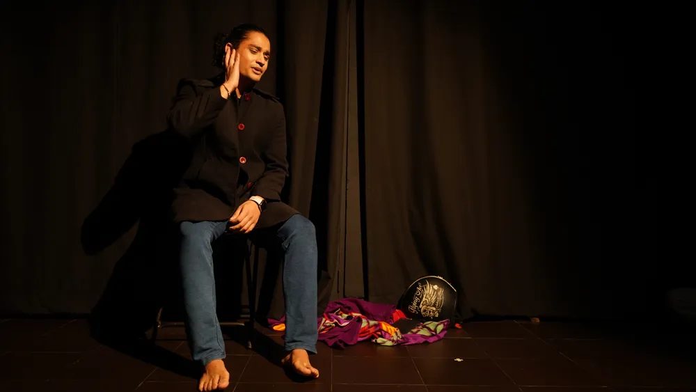 A seated performer in a black coat and red buttons